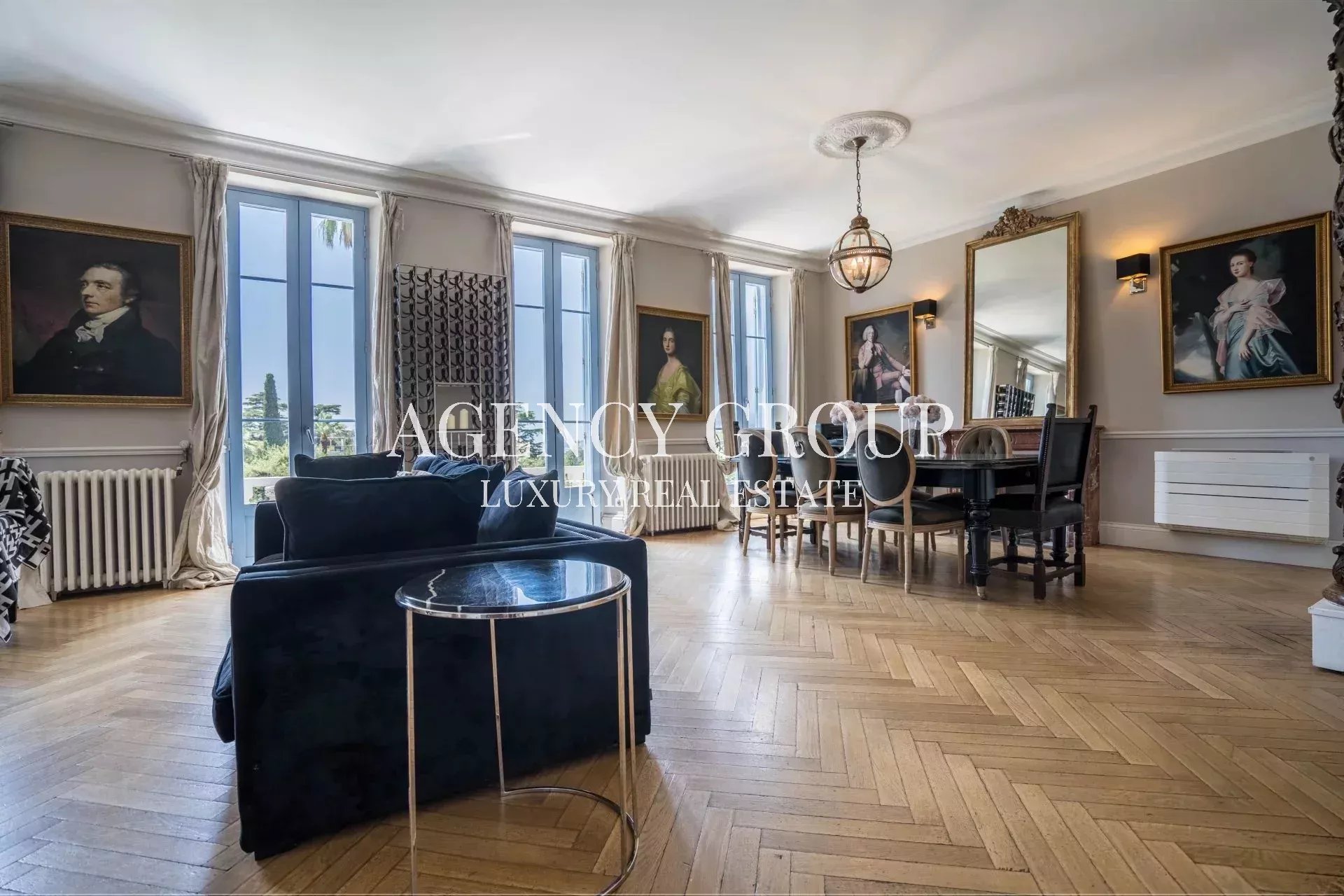Luxurious living and dining room with a blue velvet sofa, round marble side table, tall windows, and a large dining table.