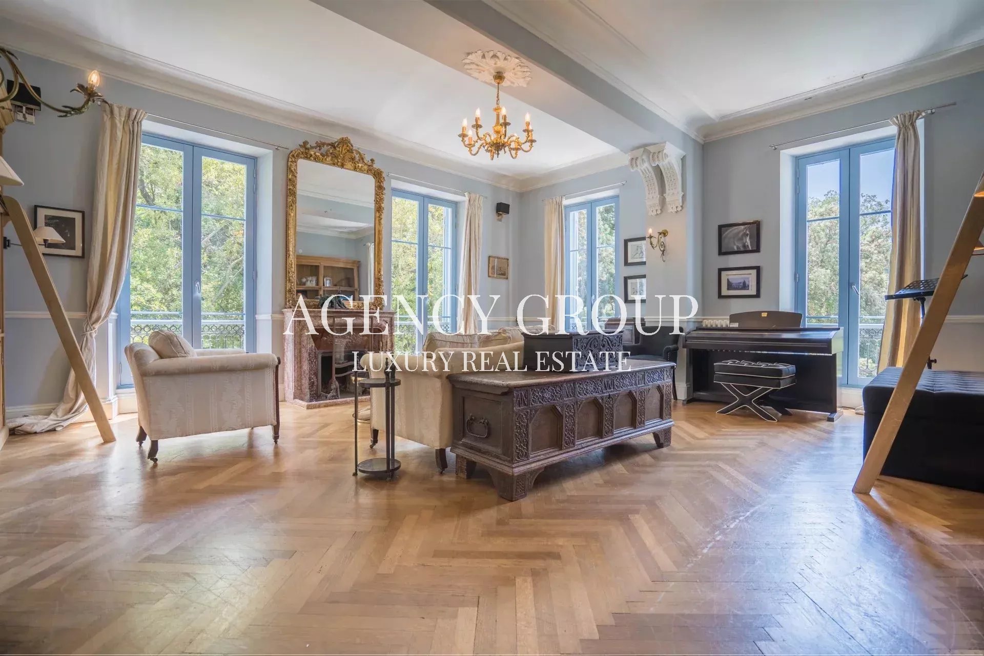 Luxurious living room with blue walls, tall windows, and an ornate chandelier over a carved wooden coffee table.
