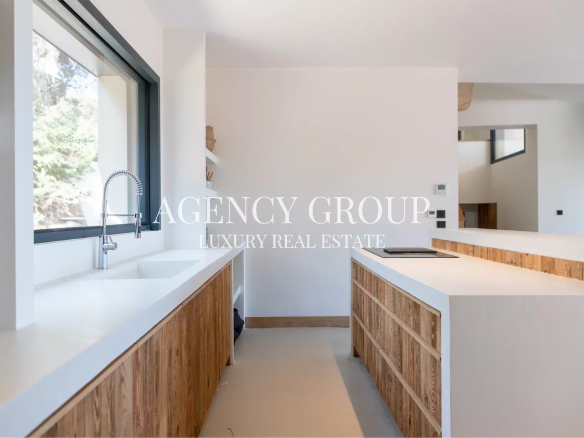 Modern kitchen with white countertops, a large window, and wood veneer cabinets along the sink wall.