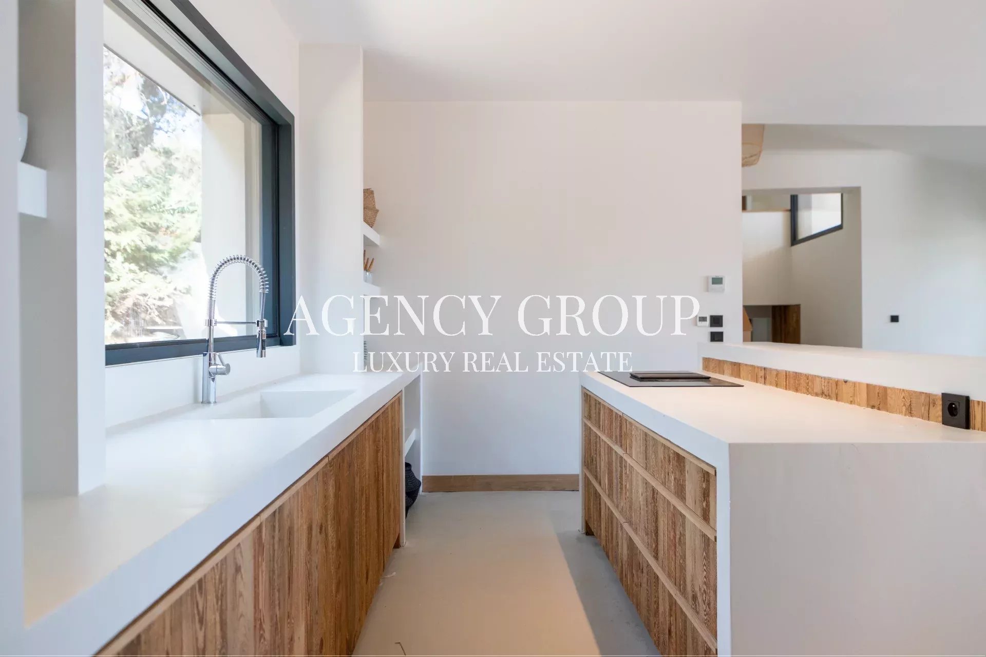 Modern kitchen with white countertops, a large window, and wood veneer cabinets along the sink wall.