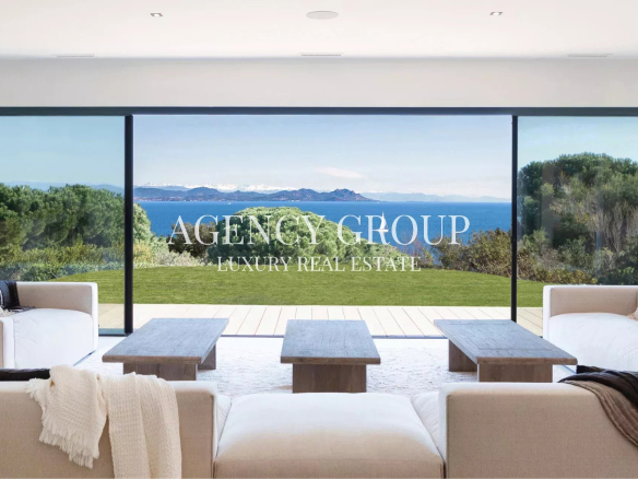 Bright living room with panoramic glass doors and ocean view; overlay reads 'AGENCY GROUP LUXURY REAL ESTATE'.