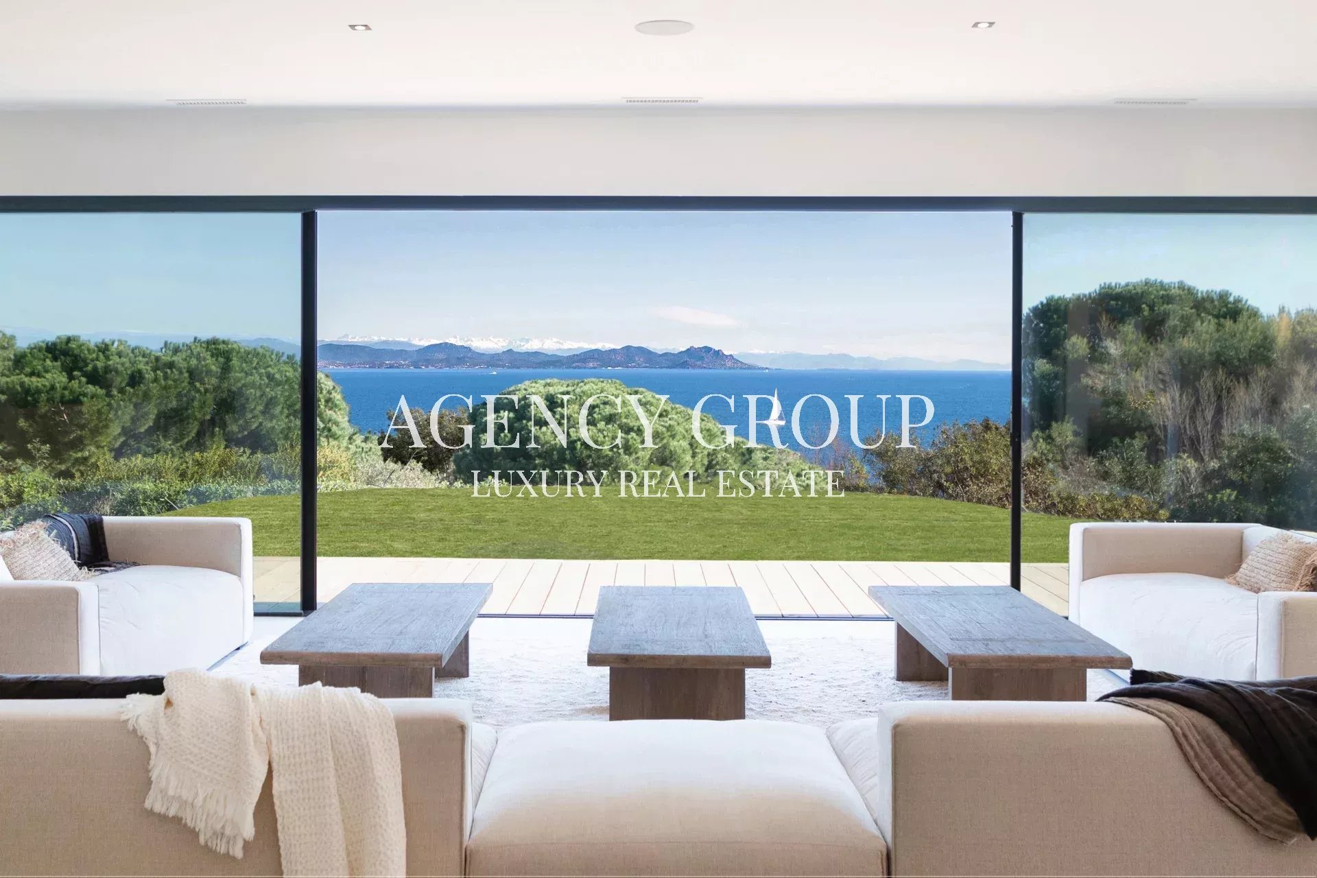 Bright living room with panoramic glass doors and ocean view; overlay reads 'AGENCY GROUP LUXURY REAL ESTATE'.