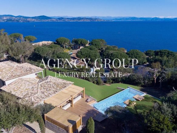 Aerial view of a luxury seaside villa complex with tiled roofs, a rectangular pool, and lush landscaped gardens overlooking the blue sea.