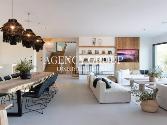 Open-plan living and dining area with a long wooden table, black chairs, and large wicker pendant lights over the dining space.