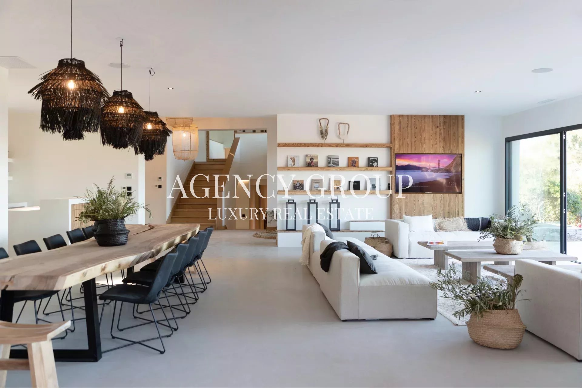 Open-plan living and dining area with a long wooden table, black chairs, and large wicker pendant lights over the dining space.