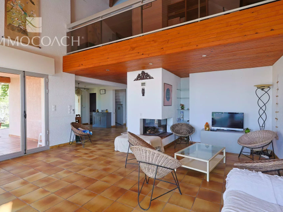 Spacious living room with terracotta tile floor, white walls, a central fireplace, and wicker chairs around a glass coffee table.