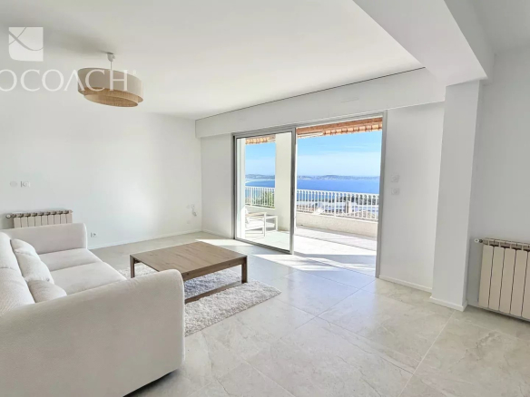 Bright living room with white sofa, wooden coffee table, and a balcony door revealing an ocean view.