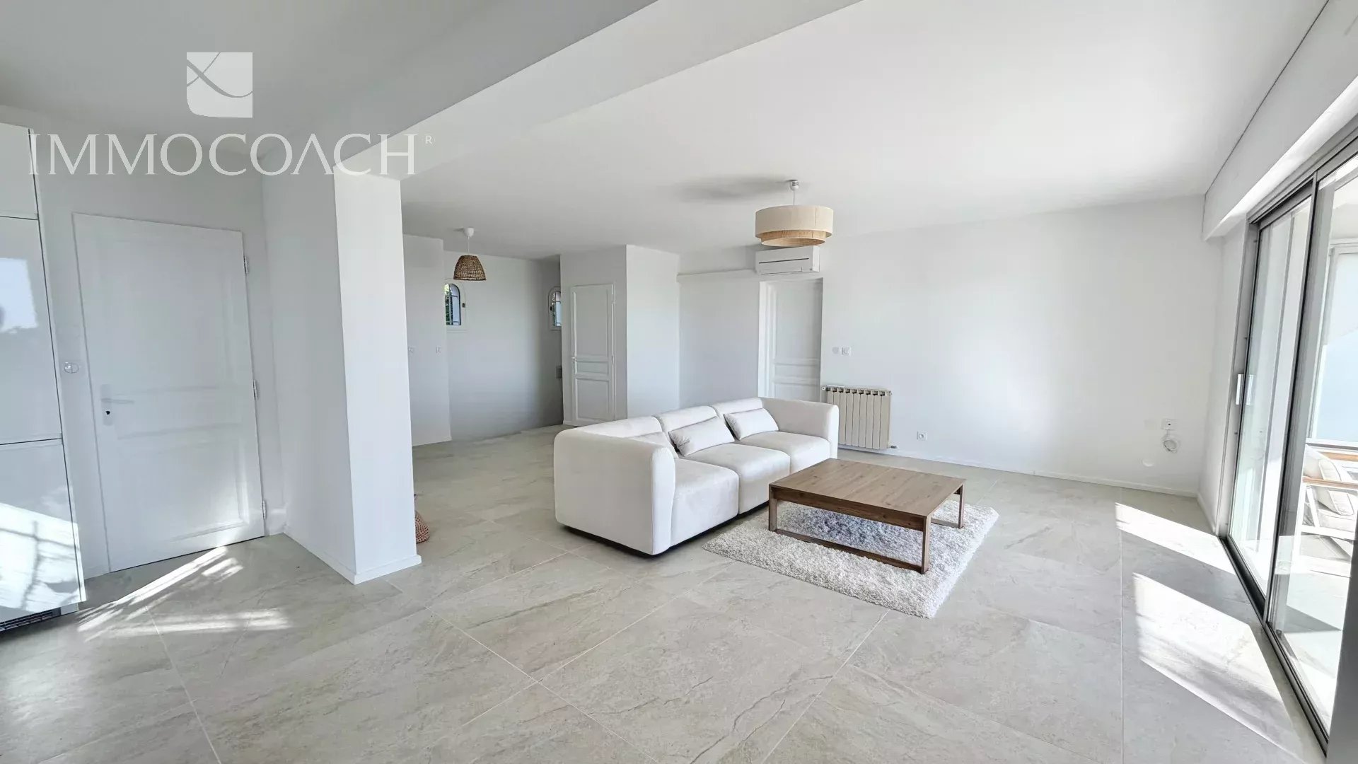 Bright open living room with a white sectional sofa, wooden coffee table, and sliding glass doors to a balcony.