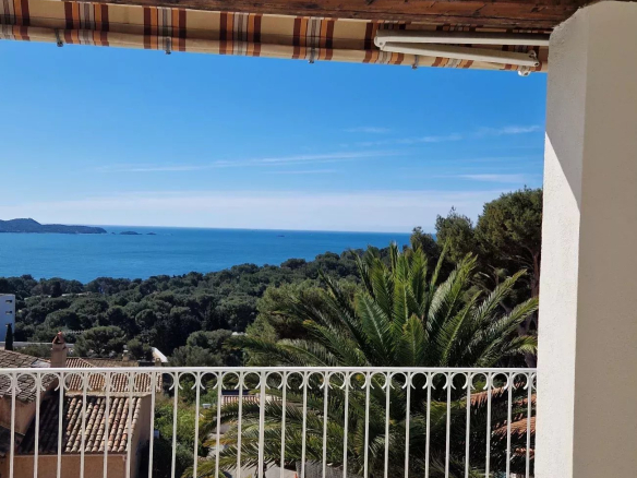 Balcony railing overlooking a blue sea with green trees and a striped awning above.