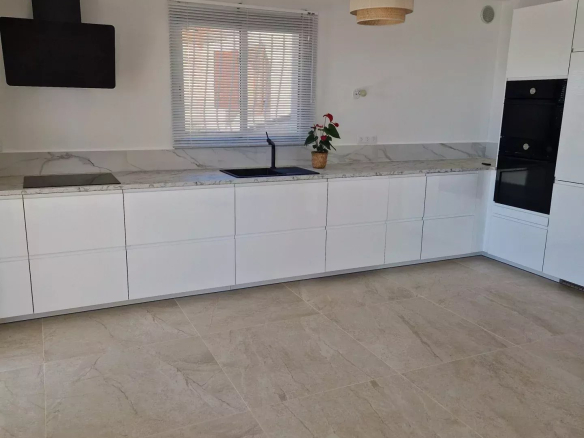 Bright modern kitchen with white handleless cabinets, marble countertop, and black wall-mounted range hood above the stove.