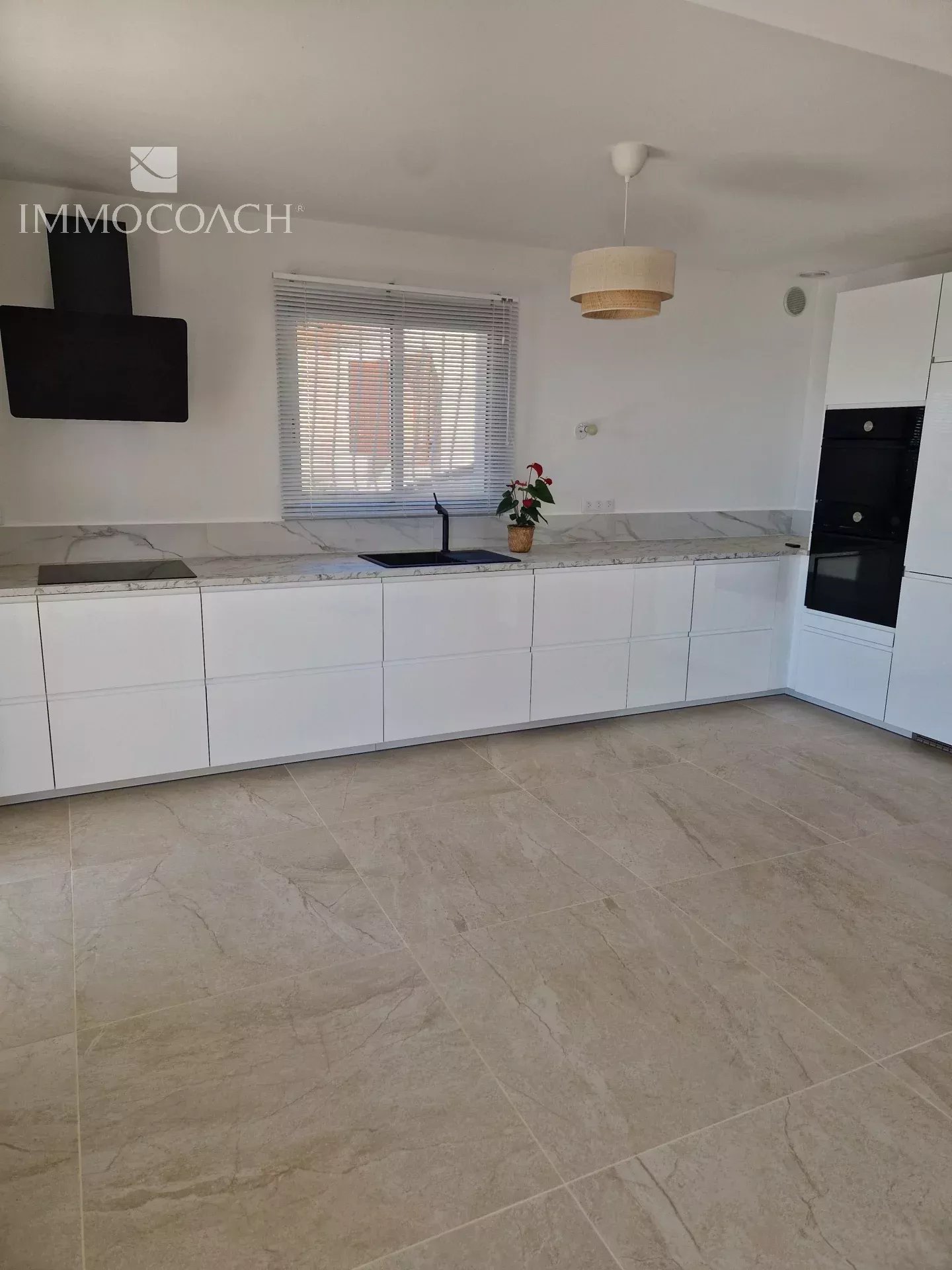 Bright modern kitchen with white handleless cabinets, marble countertop, and black wall-mounted range hood above the stove.