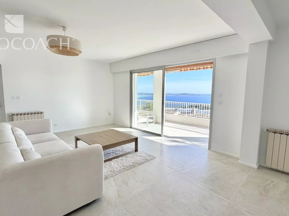 Bright living room with white sofa and wooden coffee table, sliding doors opening to a balcony with ocean view.