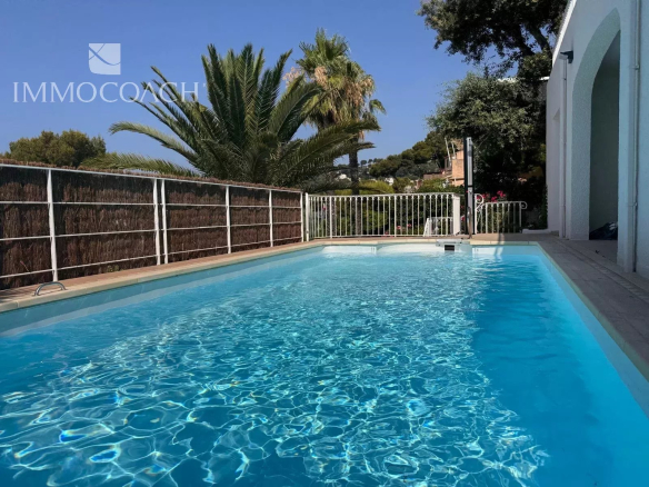Rectangular backyard pool with clear turquoise water, white railing, and palm trees under a blue sky.
