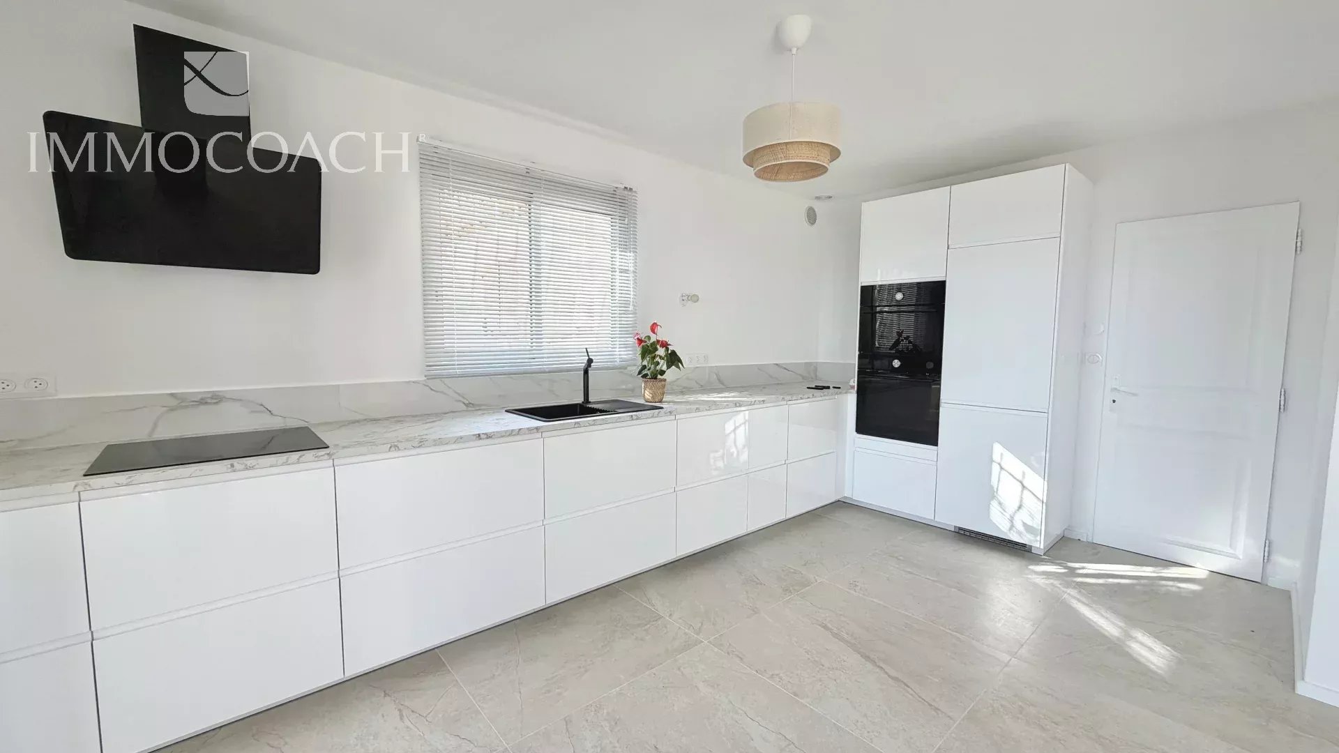 Bright white minimalist kitchen with marble countertops, long handleless cabinets, and a built-in oven cluster.