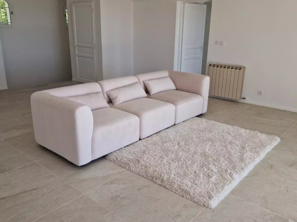 Bright minimalist living room with a light beige sectional sofa, fluffy white rug, and tiled floor.