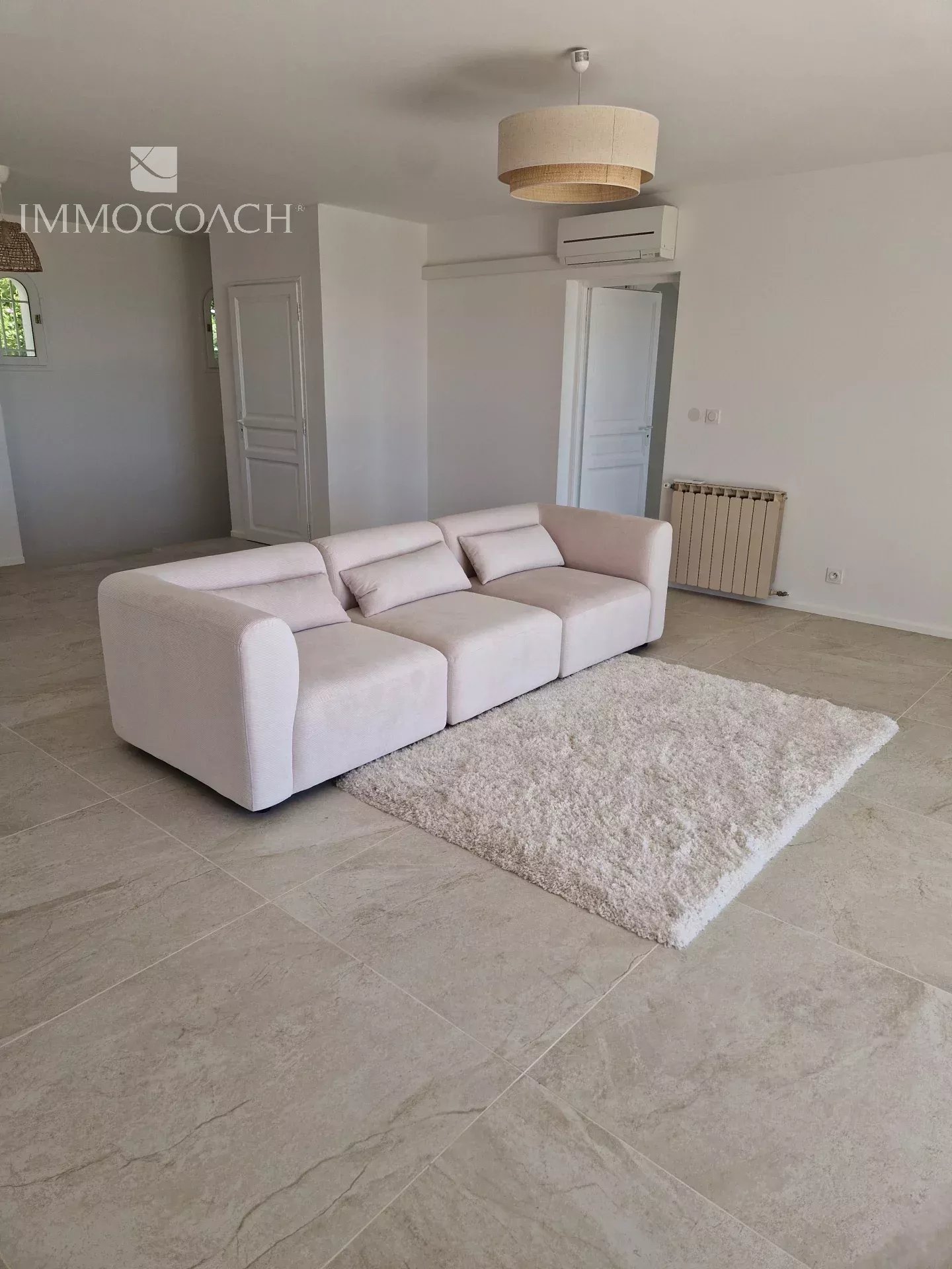Bright minimalist living room with a light beige sectional sofa, fluffy white rug, and tiled floor.