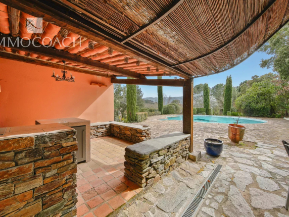 Covered stone-walled patio with terracotta tiles overlooking a rectangular pool and Mediterranean garden.