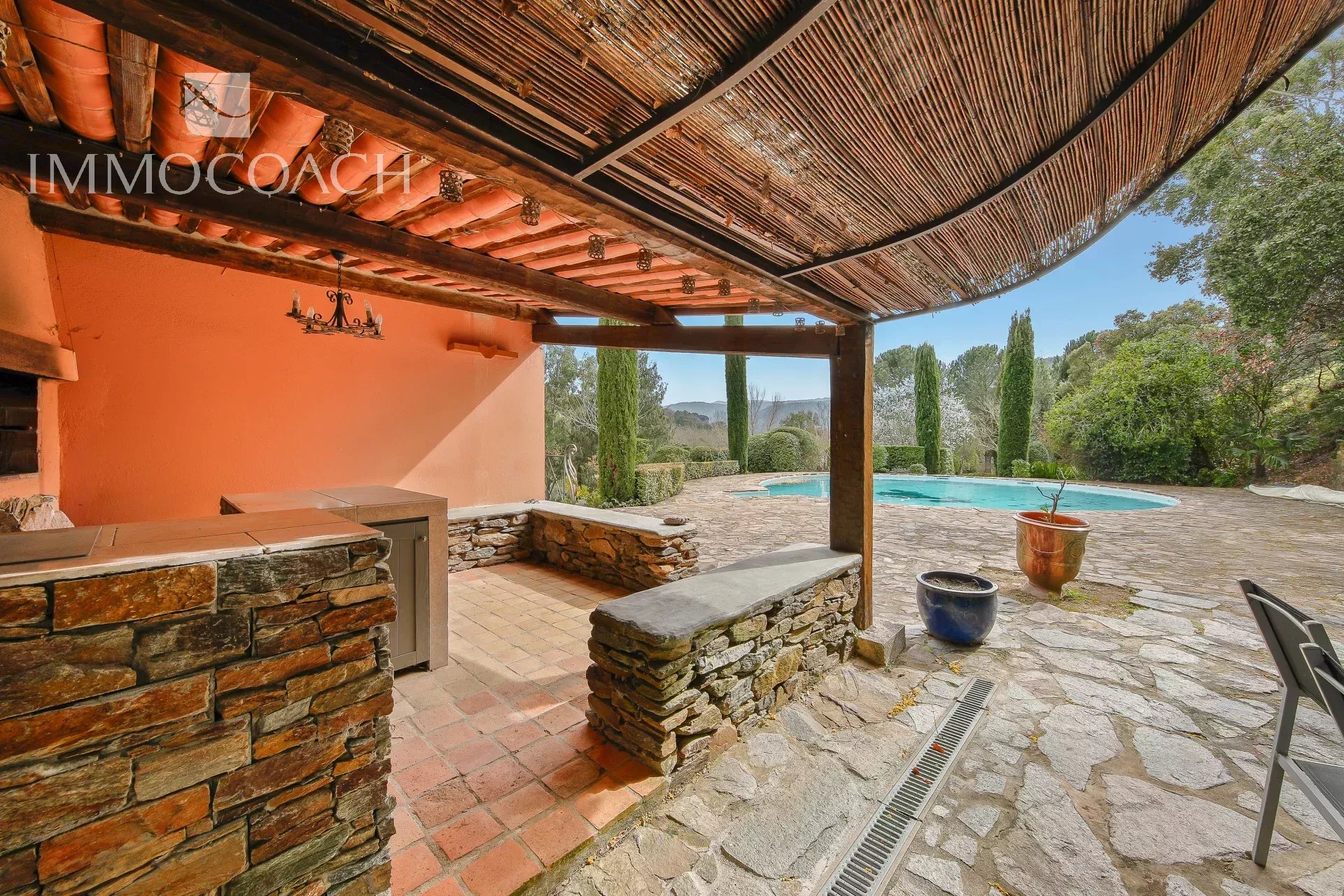 Covered stone-walled patio with terracotta tiles overlooking a rectangular pool and Mediterranean garden.