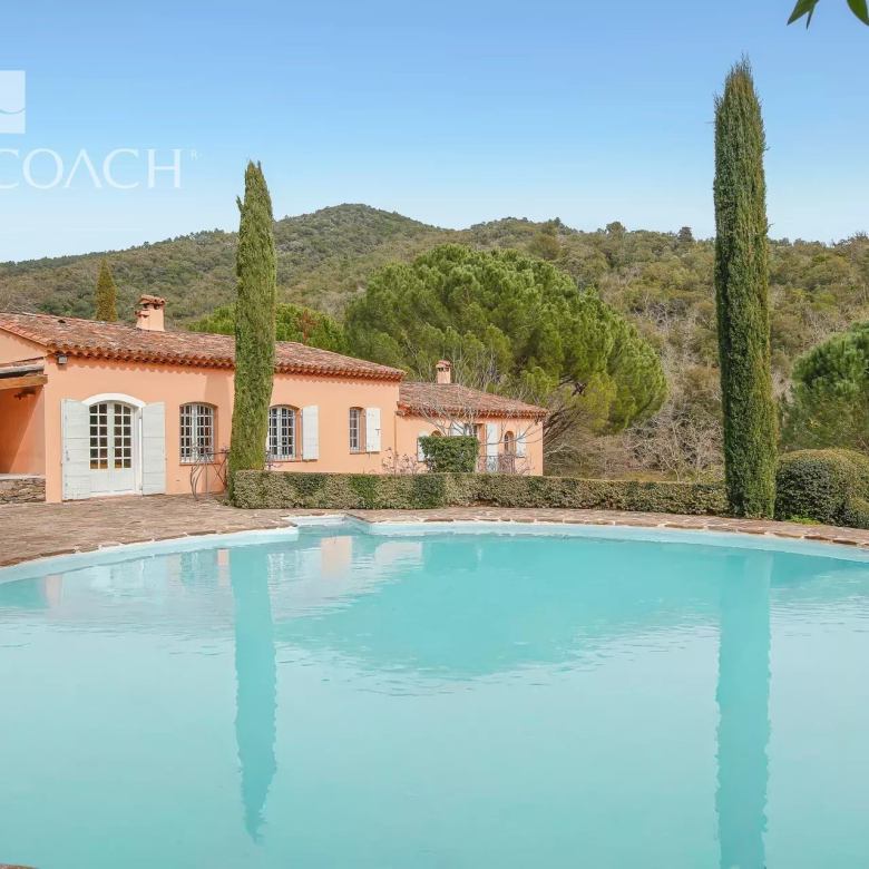 Mediterranean villa with peach exterior, white shutters, and a large circular turquoise pool in the foreground.