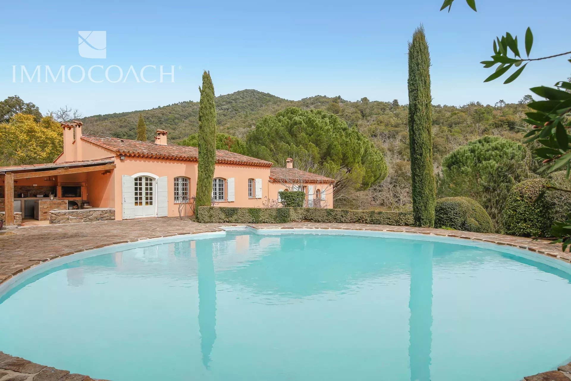 Mediterranean villa with peach exterior, white shutters, and a large circular turquoise pool in the foreground.
