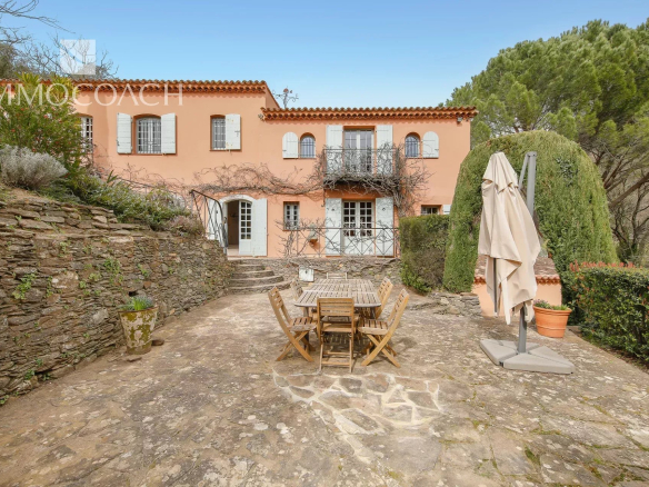 Mediterranean peach-colored villa with white shutters and a stone courtyard with a wooden dining set.