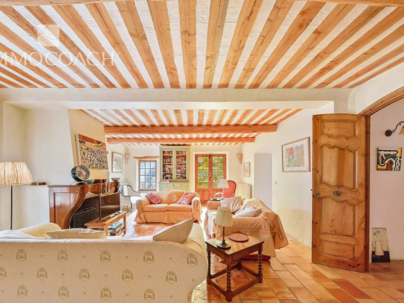 Cozy living room with exposed wooden ceiling beams, terracotta floor, and beige sofas.