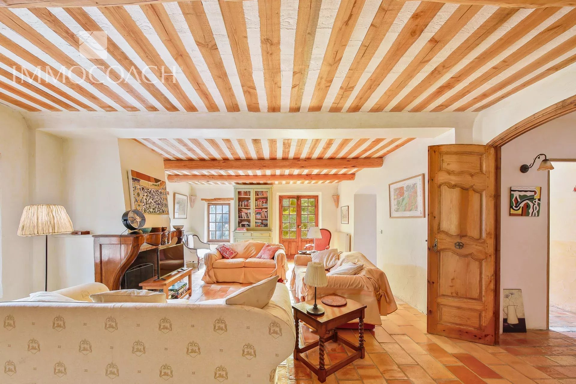 Cozy living room with exposed wooden ceiling beams, terracotta floor, and beige sofas.