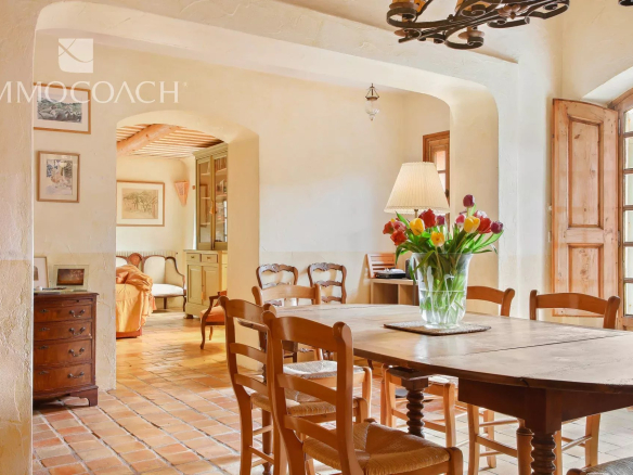 Cozy rustic dining room with a large wooden table, vase of tulips, and warm natural light from a window with shutters.