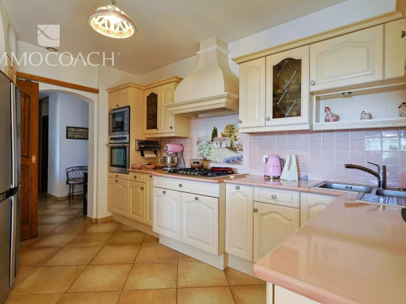 Bright cream kitchen with pastel pink accents: tiled pink backsplash, pink kettle and mixer, and cream cabinets along a galley work area.