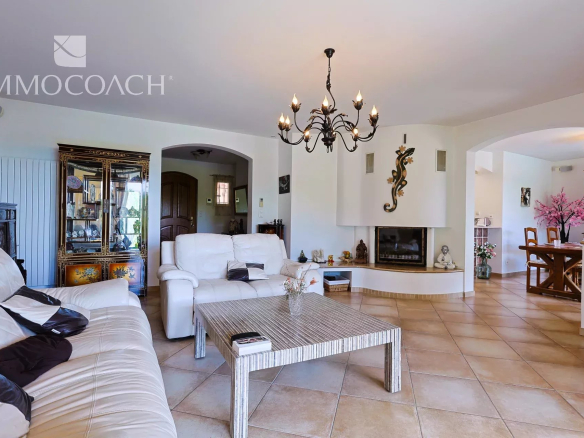 Bright living room with white leather sofas, a striped metal coffee table, and a decorative chandelier overhead.