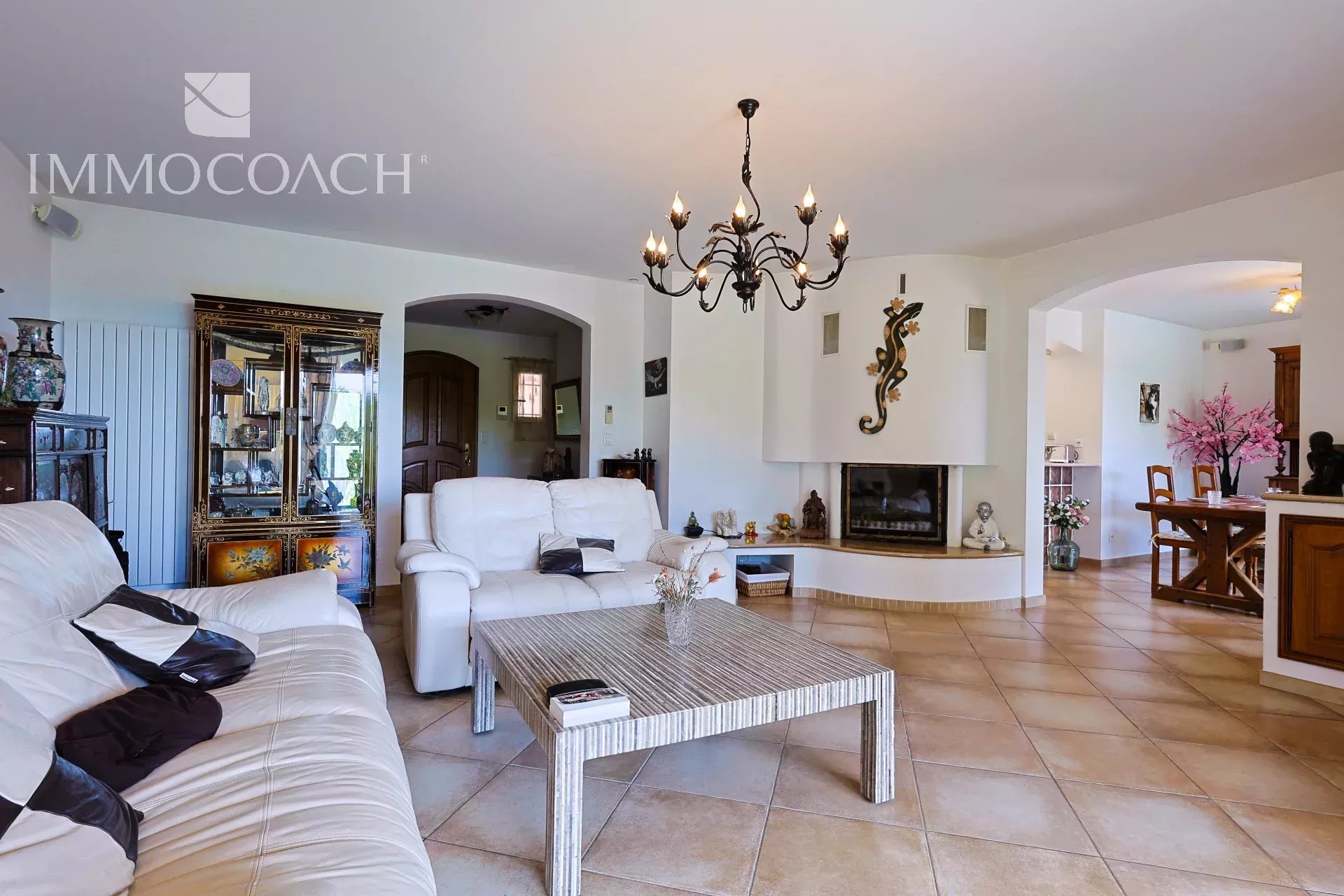 Bright living room with white leather sofas, a striped metal coffee table, and a decorative chandelier overhead.
