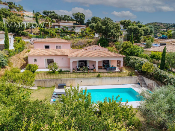Pink Mediterranean-style villa with tiled roof and a rectangular blue pool in the yard, surrounded by trees and hills.