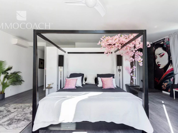 Modern bedroom with a black four-poster bed, white bedding, and pink accent pillows under a bright, airy showroom glow.