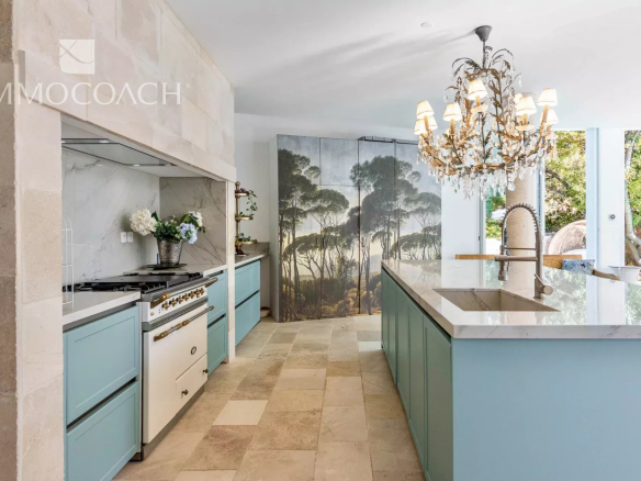 Bright kitchen with blue cabinets, marble countertops, and a large island featuring a modern brass faucet and crystal chandelier.