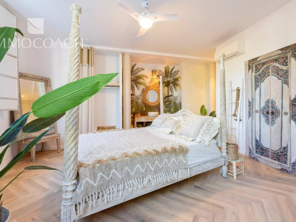 Boho-style four-poster bed with a cream knitted throw in a bright tropical-themed bedroom with plants and wicker accents.