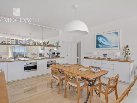 Bright open-plan kitchen and dining area with white cabinets, wooden table, and a large white dome pendant light above.