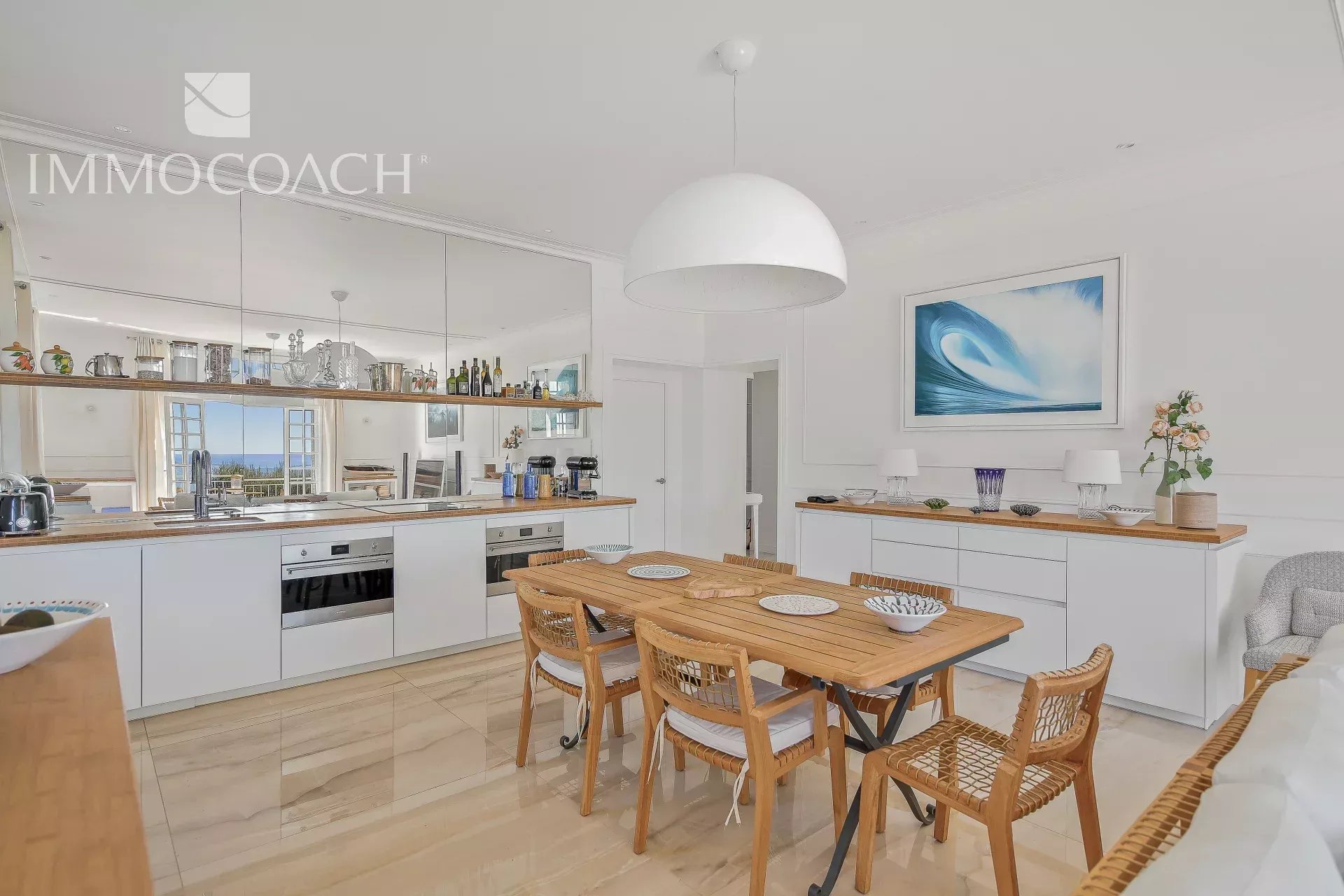 Bright open-plan kitchen and dining area with white cabinets, wooden table, and a large white dome pendant light above.