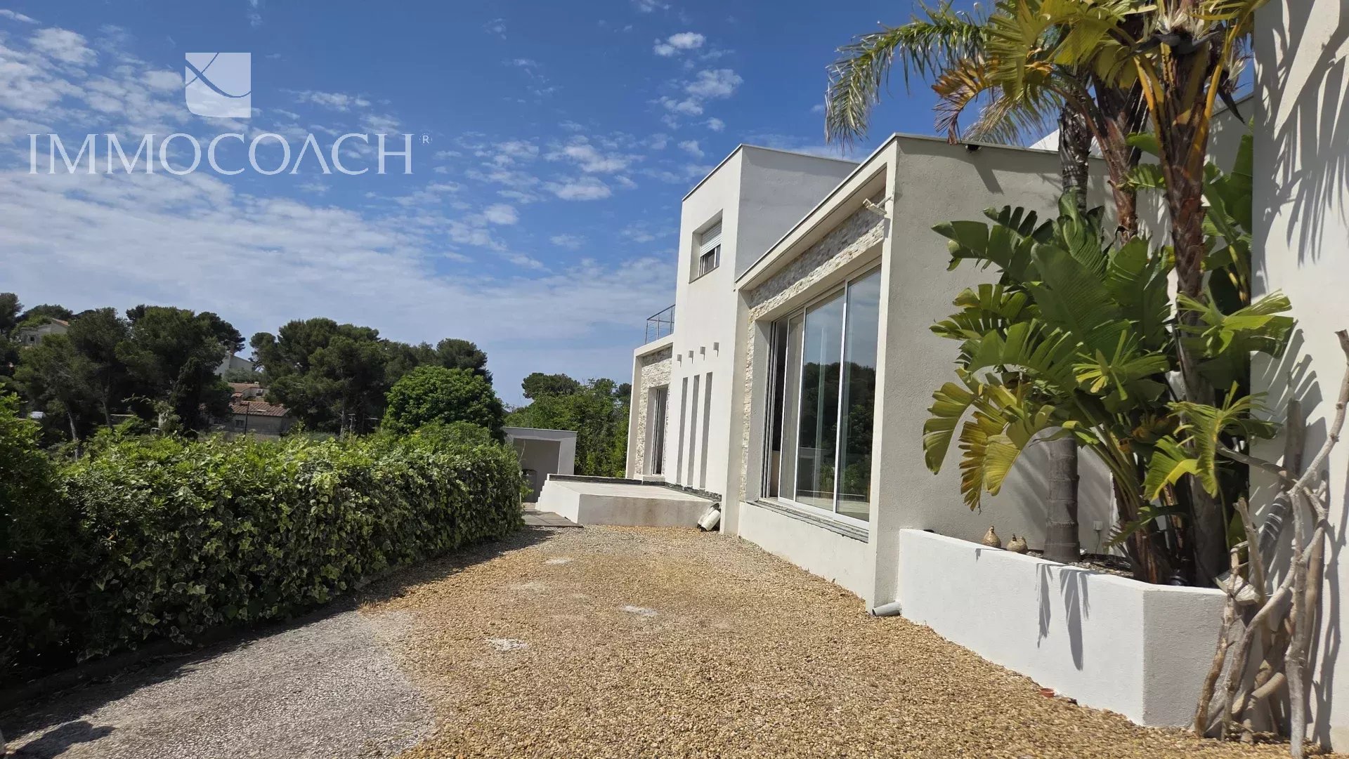 Maison contemporaine à Carqueiranne avec vue sur la mer et collines, entourée de verdure.