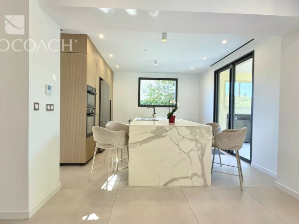 Intérieur d'une cuisine moderne avec îlot central et chaises, lumière naturelle, rénovée en 2026 à Hyères.