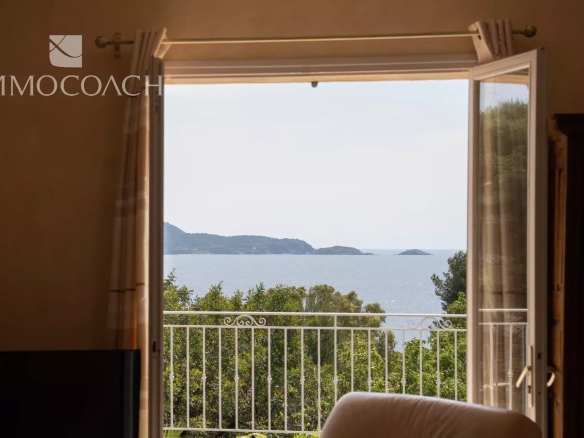 Sea view from a window with a balcony, surrounded by greenery.
