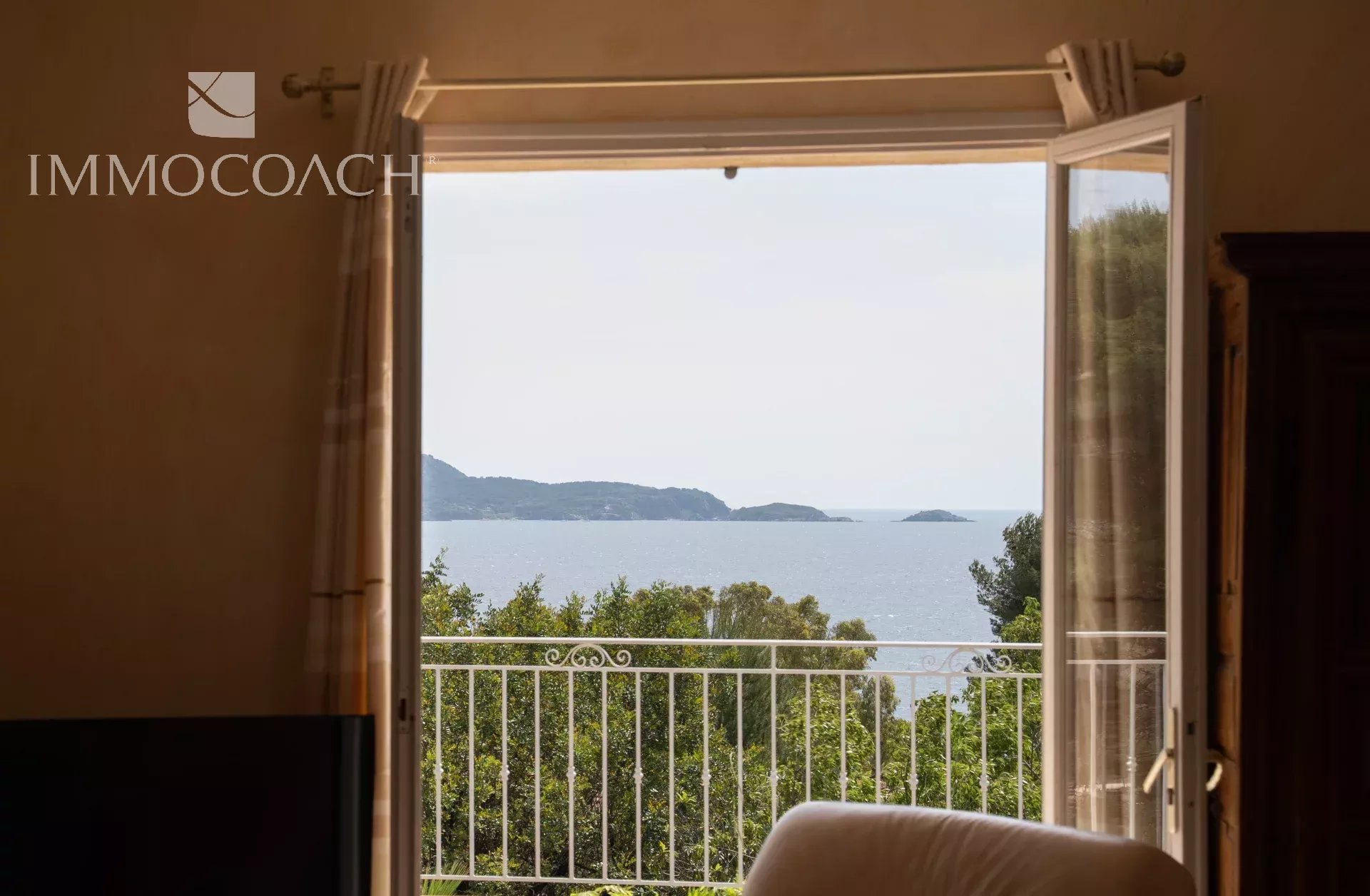 Sea view from a window with a balcony, surrounded by greenery.