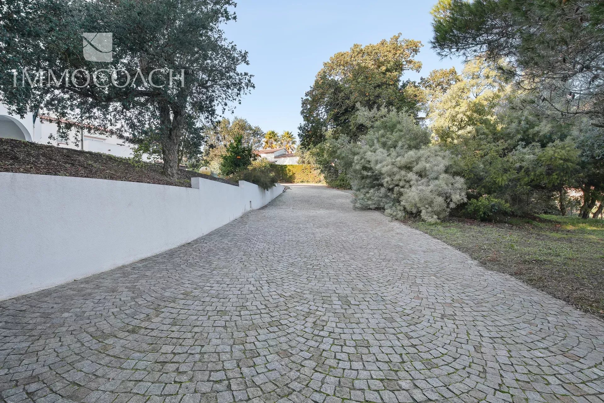 Driveway to a property in Bormes-les-Mimosas Paved driveway leading to a property with trees and a rural setting.