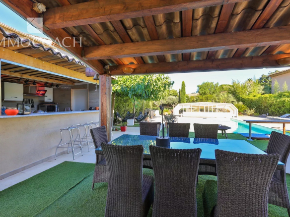 Terrasse couverte avec table et chaises, piscine et jardin en arrière-plan.