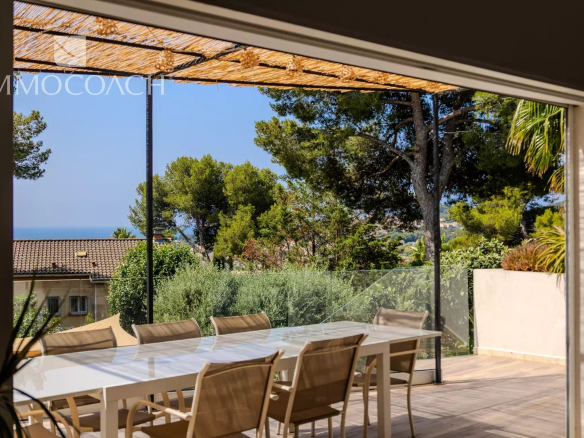 Vue d'une terrasse avec une table à manger et des chaises, entourée de verdure et d'arbres à Carqueiranne.