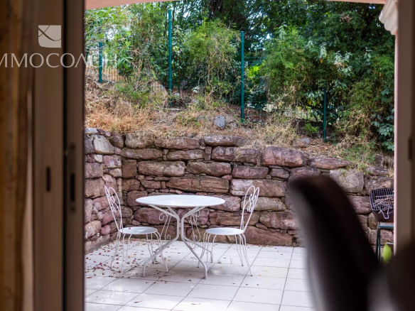 Terrasse avec table et chaises, vue sur un mur en pierre et végétation.