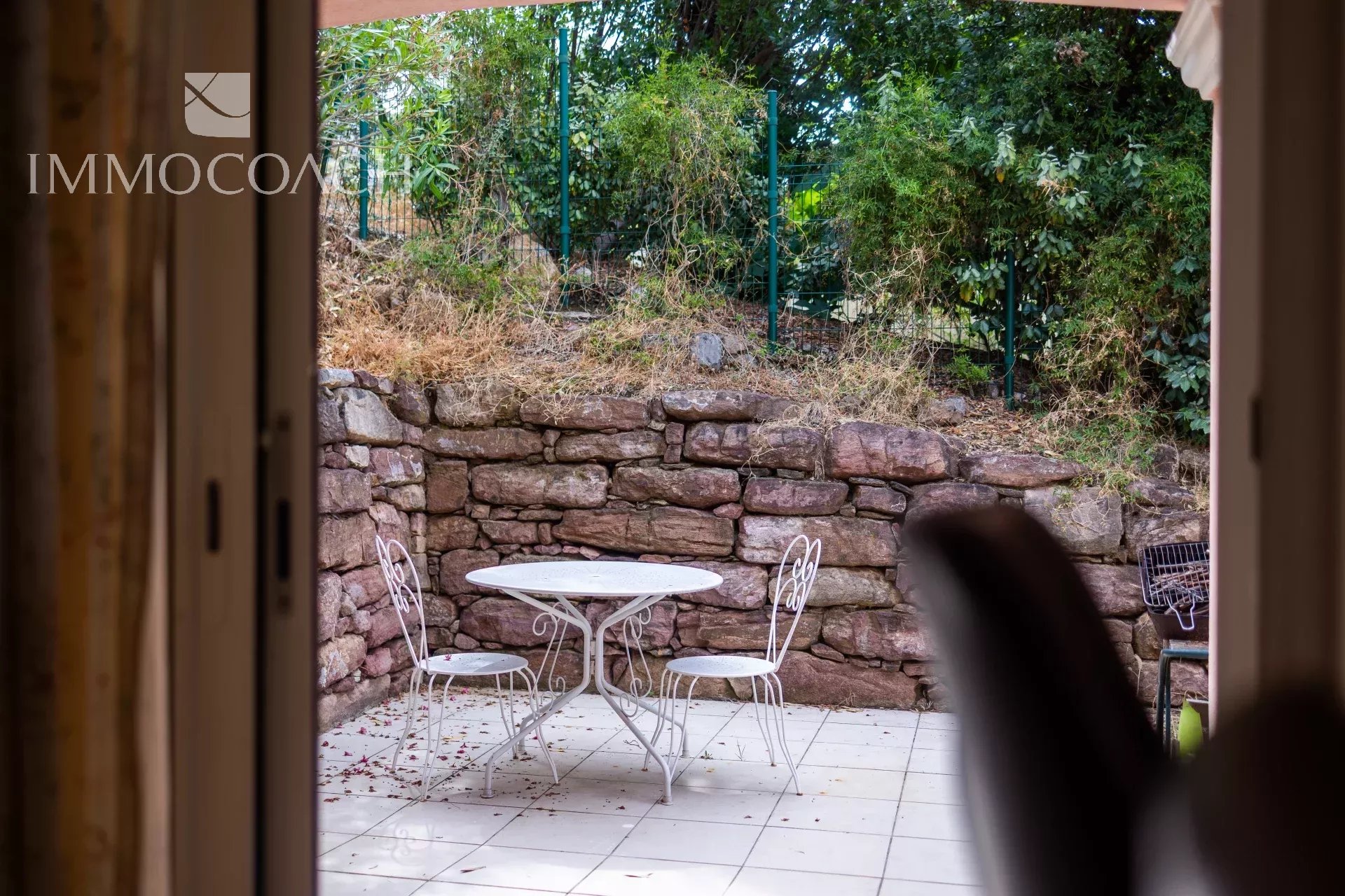 Terrasse avec table et chaises, vue sur un mur en pierre et végétation.