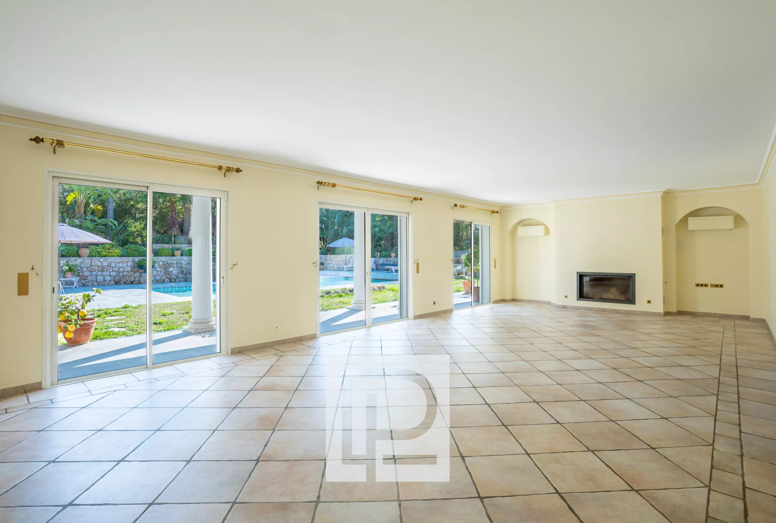 Bright empty living room with beige tiled floor and sliding glass doors to a pool and garden outside.