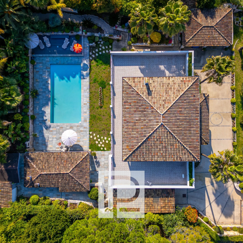Aerial view of a villa with a rectangular swimming pool, tiled patio, and surrounding palm trees and lawn areas.