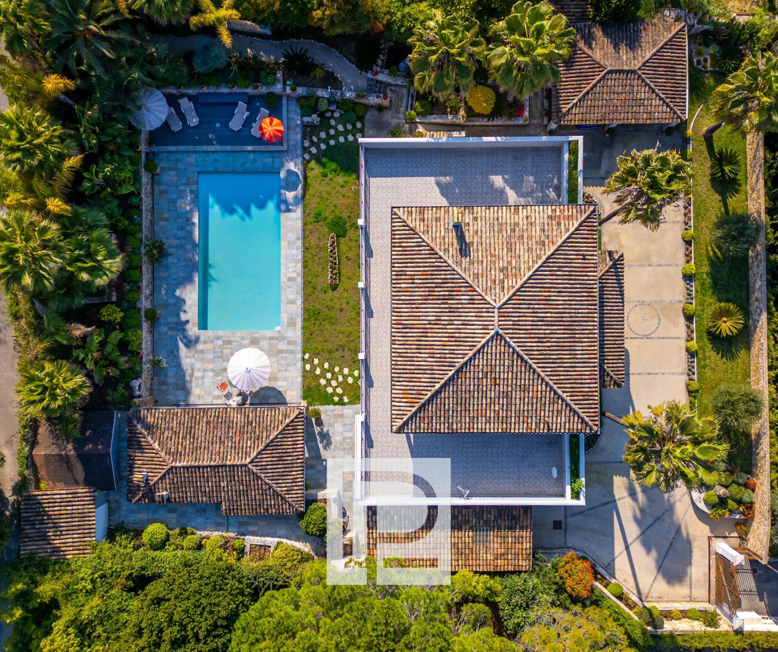 Aerial view of a villa with a rectangular swimming pool, tiled patio, and surrounding palm trees and lawn areas.
