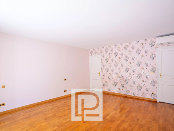Empty room with pale pink walls, a floral wallpaper accent wall, hardwood floor, two white doors, and an air conditioner above the right door.